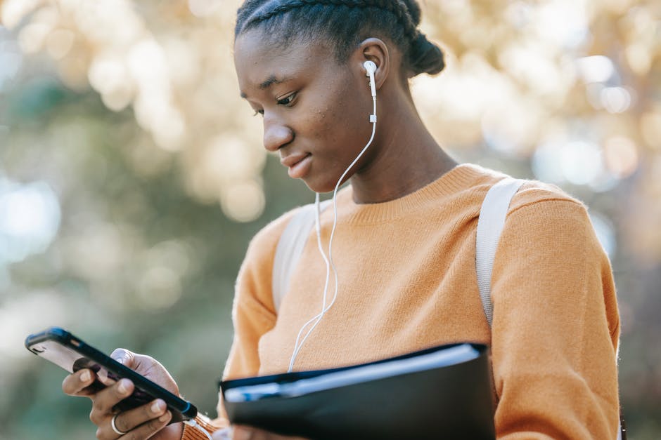 Black student listening to music using smartphone in park · Free Stock ...